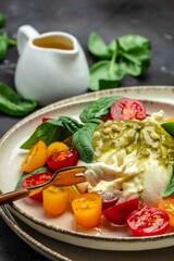 Burrata cheese with tomatoes and green pesto. Vegetarian italian food. Food recipe background. Close up