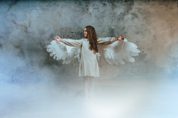 Little girl in ethnic dress wearing angel wings standing in white smoke