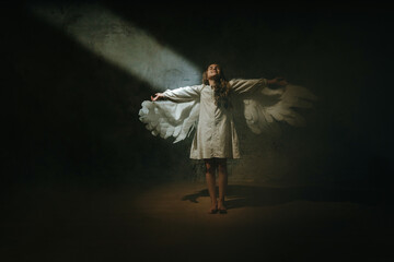 Little girl in ethnic dress wearing angel wings standing in the darkness