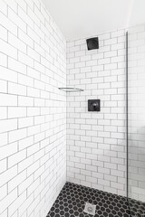 A white subway tile shower with a black shower head and a black marble tile floor.