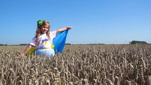 Little girl with the Ukrainian flag in the field. Child girl with the flag of Ukraine in the field of wheat. The concept of freedom, independence, peace.