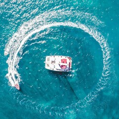 Aerial view of a speed boat towing around a sailing catamaran yacht in Guadeloupe of the Caribbean