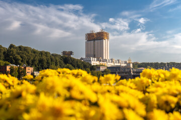 Skyscraper adorned with golden structure on roof and bright yellow flower bed, Moscow, Russia