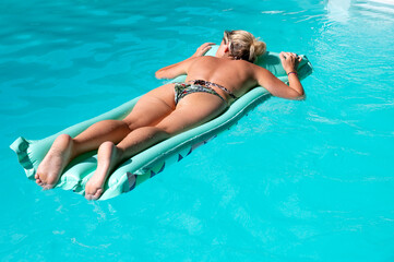 Femme blonde allongée sur le ventre en train de bronzer sur un matelas pneumatique dans une piscine bleue