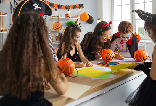 Arts And Crafts Studio Leader Enjoying Drawing Activity With Children. English Language Teacher And Kids Dressed As Pirates, Witches And Vampires Having Fun Halloween Traditions Culture Studies Class