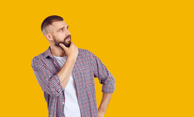 Young man has doubts about something. Confused guy in casual shirt standing isolated on yellow...