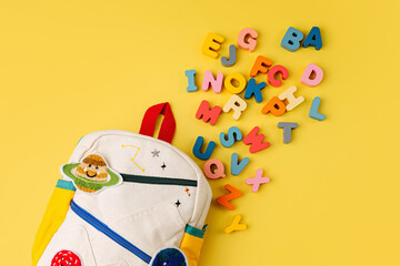 Opened Kids backpack with letters of the alphabet. Primary school or preschool, kindergarten. School Backpack on yellow background.