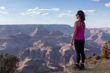 Naklejka premium Adventurous Traveler standing on Desert Rocky Mountain American Landscape. Cloudy Sunny Sky. Grand Canyon National Park, Arizona, United States. Adventure Travel