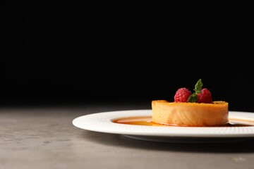 Delicious pudding with caramel and raspberries on grey table against black background. Space for text