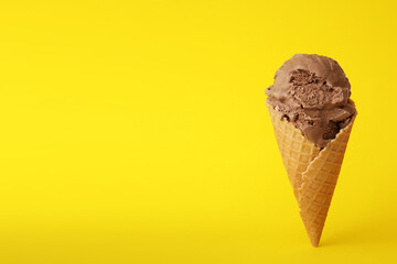 Delicious chocolate ice cream in waffle cone on yellow background. Space for text
