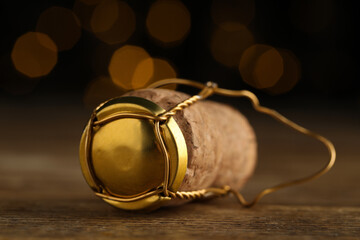 Cork of sparkling wine and muselet cap on wooden table against blurred festive lights, closeup....