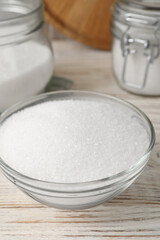 Granulated sugar in glass bowl on white wooden table, closeup
