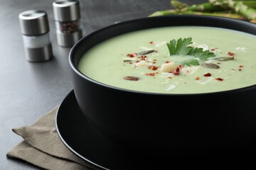 Bowl of delicious asparagus soup on dark table, closeup
