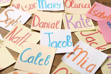 Paper notes with different baby names on wooden table