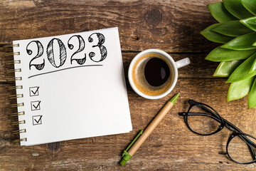 New year goals 2023 on desk. 2023 goals list with notebook, coffee cup, plant on wooden table....