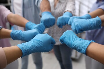 People in blue medical gloves joining fists indoors, closeup