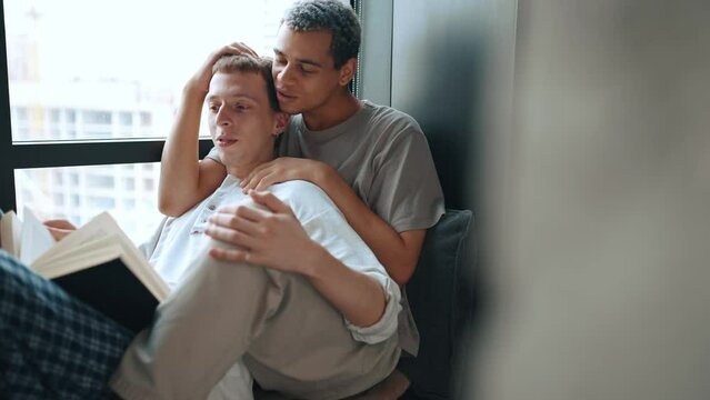 Lovely multinational gay couple reading book and talking at home