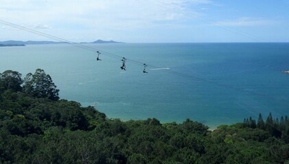Beautiful shot of people on a zipline over the sea and greenery
