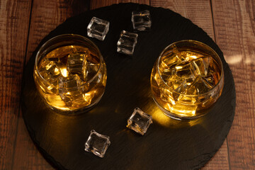 two liqueur glasses of whiskey, rum, etc., lit liqueur from inside the glass with ice cubes tray or stone plate slate wooden table