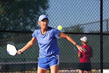 A senior woman serves during a ladies pickleball match.