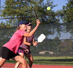 Pickleball being played, outdoors, by ladies.