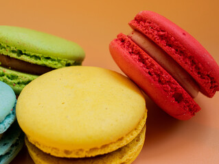 Close-up of French dessert for coffee. Multicolored macarons or macaroons on orange background....