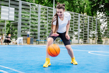 Young athletic woman is training to play basketball on modern outdoor basketball court. Happy woman