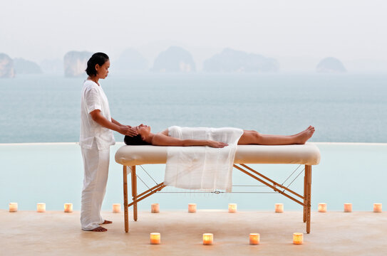 A woman receives a candlelit poolside massage at dusk at a  three-bedroom private pool villa. Yao Noi. Thailand.