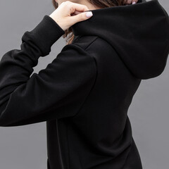 Black hoodie on woman. Long warm sleeve and patch pocket. Clothing for autumn or winter on gray background