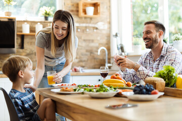 Happy mother talking to her small son while giving him orange juice during lunch time at dining table