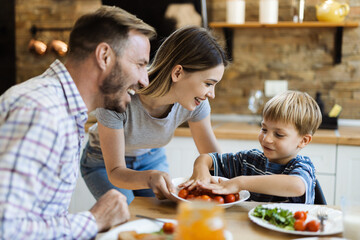 Happy mother serving food to her family while father and son having fun in dining room