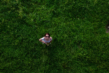 Portrait of happy cute young woman with short hair in casual black and white striped shirt, red round eyeglasses lying down on green grass and looking at camera through glasses.outdoor summertime shot