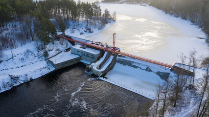Aerial view of hydroelectric power plant in the river surrounded by dense trees in winter