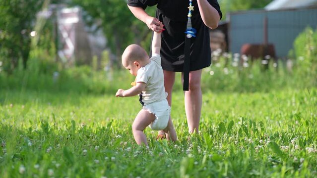 Mom and baby walk hand in hand on the green grass. Baby first step outdoor walking. 
