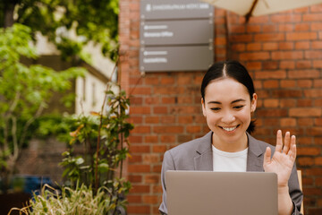 Asian young woman smiling while using laptop in cafe outdoors