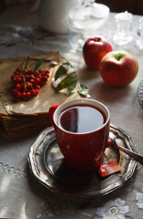 A cup of tea with a bunch of red rowan and red apples, autumn morning tea concept.