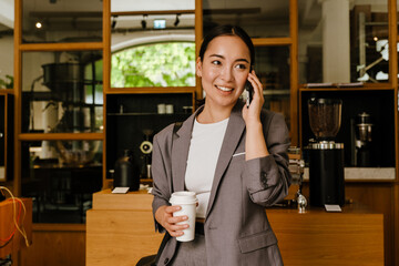 Asian businesswoman drinking coffee and talking on cellphone in cafe