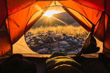 sleeping bag inside an orange tent in the mountains in a sunset surrounded by rocks and yellow vegetation in the winter in the andes mountain range