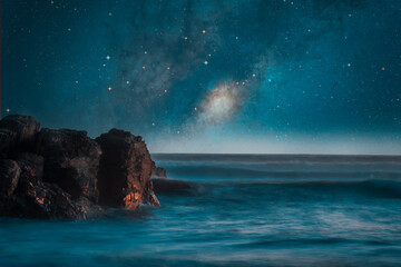 milky way over the sea and rocks on the shore background