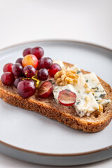 Toasted bread with mild creamy blue cheese, grapes and walnuts on grey plate