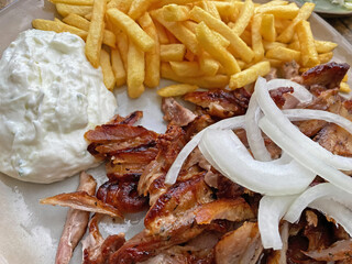 Closeup of isolated ready to eat greek pork gyros plate with onions, french fries and tzatziki dip