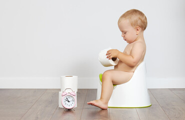 Cute baby boy sits on the potty with toilet paper in his hands. Potty training time