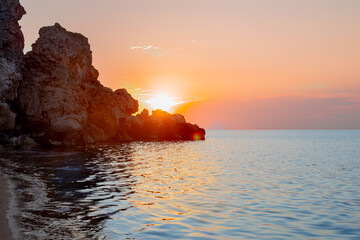 Seascape. Sunset on the sea rocky coast with the sun going behind the mountain.