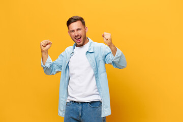 Happy overjoyed tanned handsome man in blue basic t-shirt raise fists up have big luck posing...