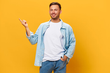 Happy cheerful tanned handsome man in blue basic t-shirt point finger aside look at camera posing isolated on yellow studio background. Copy space Banner Mockup. People emotions Lifestyle concept