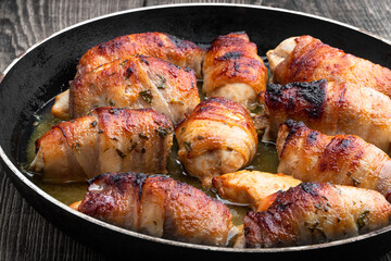 Chicken breasts wrapped in bacon in frying pan on wooden table