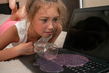 A child spilled juice on a laptop keyboard. A little girl accidentally spills a drink on the computer.