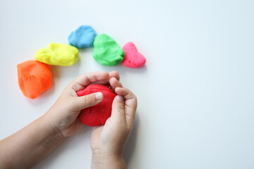 Baby hands holding and kneading red modeling clay on white table background. Closeup. Toddler development. Preparing material for making different colorful shapes