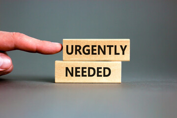 Urgently needed symbol. Concept words Urgently needed on wooden blocks on a beautiful grey table grey background. Businessman hand. Business and urgently needed concept. Copy space.