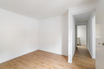 Fototapeta na wymiar Empty room with laminate flooring and newly painted white wall in refurbished apartment with corridor leading to bathroom. Repair and construction concept.